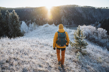 Rear view of man with backpack on hiking trip, solo trekking in the mountains, hiking with backpack in nature in winter season.