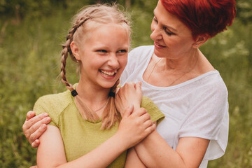 A mother is hugging her teenage daughter from behind, both are laughing