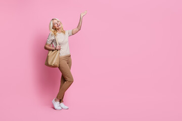 Full length portrait of gorgeous positive person hold bag hand demonstrate empty space isolated on pink color background