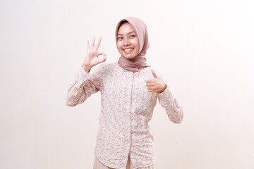 Satisfied young asian muslim woman standing while showing okay and thumbs up hand gesture