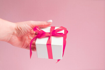 white gift box with pink ribbon bow in woman hand with white sweater with copy space.
