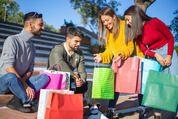 Two young couples enjoy shopping. Two girls show their purchases in the various colorful shoppers...