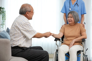 Obraz premium senior woman sitting on wheelchair and holding hands senior man together beside caregiver at home