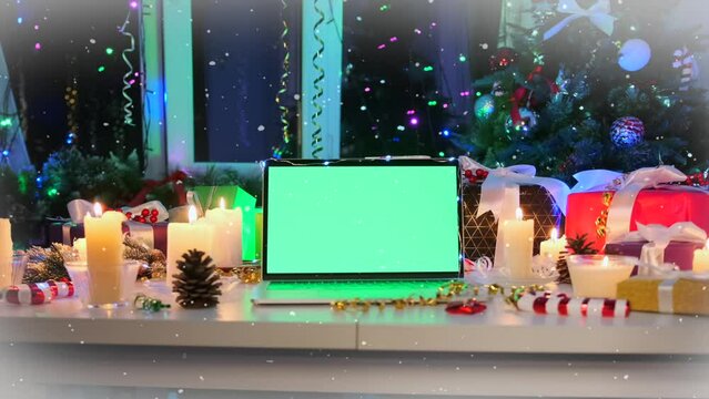 Open laptop with green chromatic screen on white table among xmas glowing candles, fluffy Christmas trees, packed gift boxes, tinsel and flickering garlands. New Year party event advertising.
