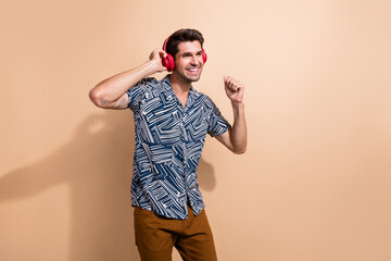 Photo of cheerful nice guy trendy print clothes listening music modern earbuds looking empty space isolated on beige color background