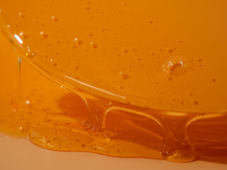 Liquid shower gel flows gracefully across a bright orange background. The translucent waves of the shower gel create a captivating visual symphony. Liquid shower gel flows over an orange background.