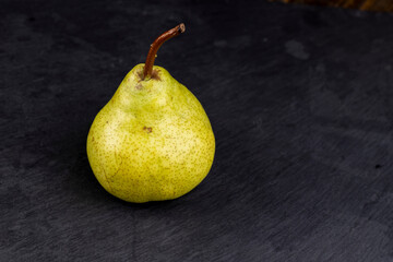 one whole green pear on a black slate board close-up