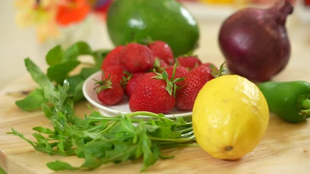 Strawberries on a plate alongside with fresh vegetables and greens as ingredients