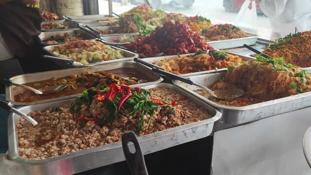 Counters with a lot of Thai dishes. A variety of exotic Asian dishes on the street, various types of dishes selling at the food stall, people can seen choosing the dishes at the stall.