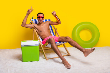 Full length photo of funny carefree masculine guy showing v-sign drinking beer tanning lounge chair...