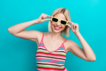 Photo of attractive nice young hipster lady touching sunglasses ray ban posing model wear knit singlet isolated on cyan color background