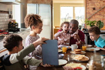 Family Fun at Breakfast Time. Father sitting with children in kitchen looking at tablet