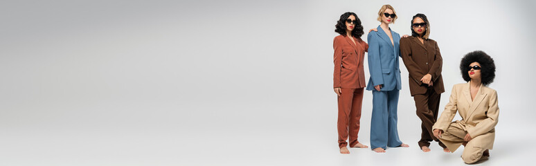 african american woman on haunches near multiethnic girlfriends in sunglasses and suits, banner