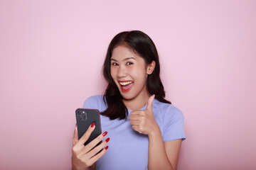 Posing alone on a light pink background. Asian woman is excited about something on the phone The...