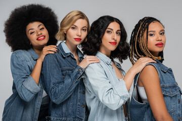 multiracial girlfriends in jeans wear holding hands on shoulders of each other and smiling at camera