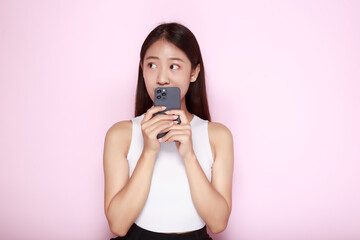 Portrait of a beautiful young woman in a light pink background, happy and smile, posting in stand position, Asian woman holding a phone in her hand.