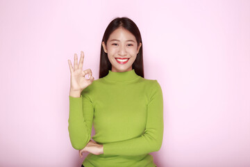 Asian woman making OK gesture with her hands, Portrait of a friendly young woman smiling happily, Portrait of a beautiful young woman in a light pink background,
