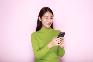 Portrait of a beautiful young woman in a light pink background, happy and smile, posting in stand position, Asian woman looks surprised while holding phone in hand