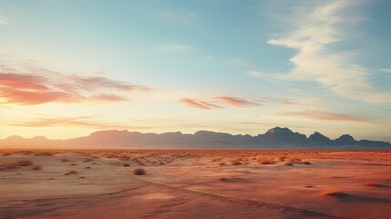  a view of a desert with mountains in the distance and a sunset in the middle of the desert with a few clouds in the sky.