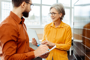 Smiling engineers, man and senior woman planning startup project, cooperation using laptop, solar panel working in modern office. Business people on meeting. Alternative energy, innovation concept