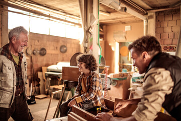 Adorable little boy working with older carpenters in workshop