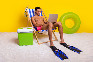 Full length photo of good mood positive masculine guy sitting lounge chair working apple samsung gadget isolated yellow color background