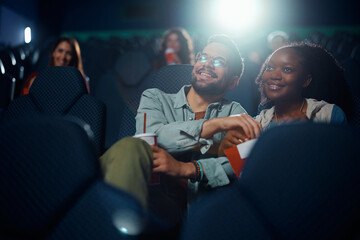Happy couple eating popcorn while watching movie projection in theater.
