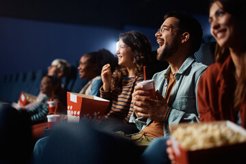 Cheerful man has fun while watching movie with friends in cinema.