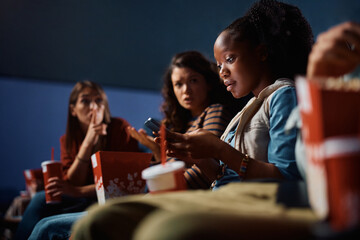 Black woman using cell phone during movie projection in cinema.