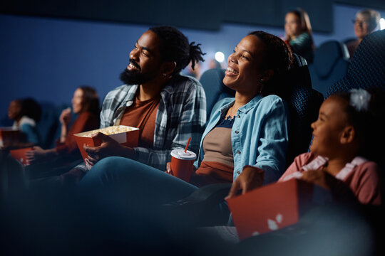 Happy black family enjoying in watching movie in cinema.