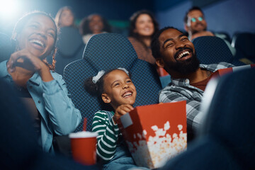 Cheerful black family having fun while watching movie in theater.