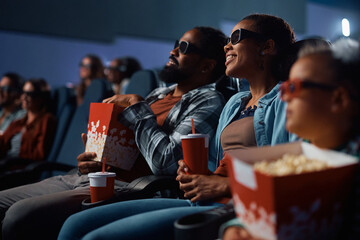 Happy black family wearing 3D glasses during movie projection in theater.