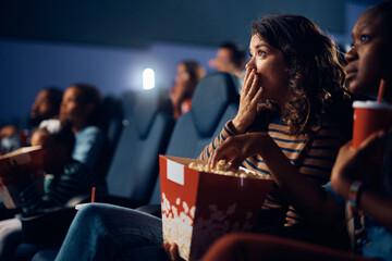 Shocked woman watching suspenseful movie in theater.