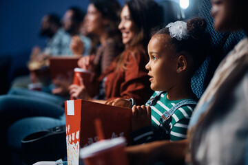black little girl eats popcorn during movie projection in cinema.