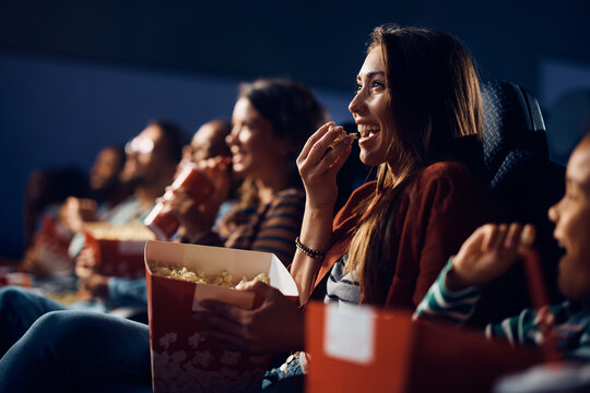 Cheerful woman eating popcorn during comedy movie in cinema.