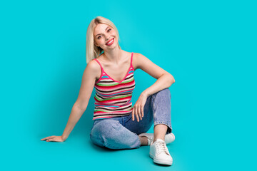 Full length photo of shiny cheerful girl dressed striped tank top sitting floor empty space isolated teal color background