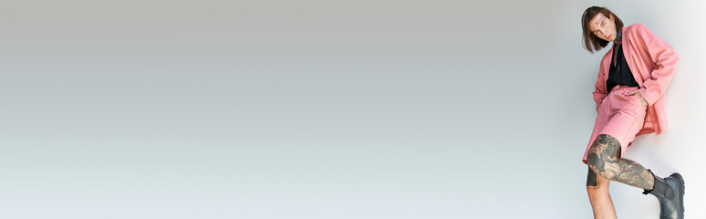 young sexy man in stylish attire with leg on wall and hands in pockets, fashion concept, banner