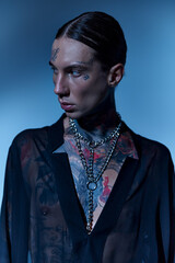 vertical shot of handsome stylish man with tattoos and piercing in transparent shirt looking away