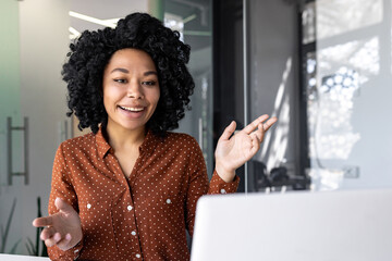 Joyful successful businesswoman talking remotely using laptop for video call, female employee smiling and gesturing looking at computer screen, working inside office at workplace.