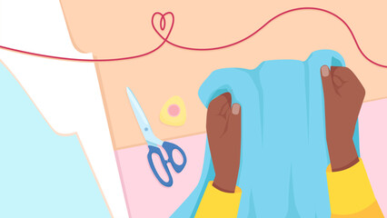 Two female dark-skinned hands hold fabric on the background of a table with sewing tools