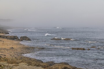 Fototapeta premium View of the turbulent and foggy Atlantic Ocean at Praia Aivados in Portugal in the morning light