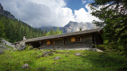 Mountain landscape. Adventure background. Small wooden cabin with mountain background. Dark building in the woods. Ecological house. Adamello group, Italy.
