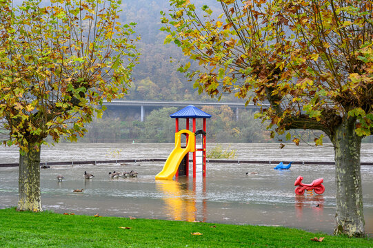 A playground framed by trees is submerged with a slide and two rocker toys on springs sitting in water after the adjacent river went over its banks due to rain fall and climate change.