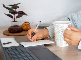 Woman working at home planning on a notebook while holding a hot drink. Freelance coffee break with...