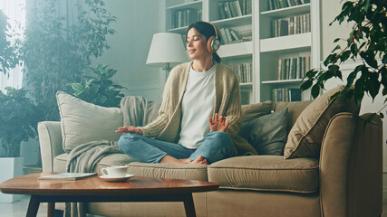 Portrait of young woman relaxing at home and listening music. Girl sitting on sofa. Relaxation, Meditation and Mindfulness - obrazy, fototapety, plakaty