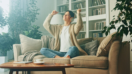 Obraz premium Portrait of young woman relaxing at home and listening music. Girl sitting on sofa. Relaxation, Meditation and Mindfulness