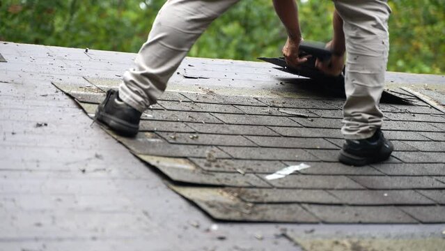 Closeup view of roofer removing old roof shingles as part of a house renovation project in slow motion