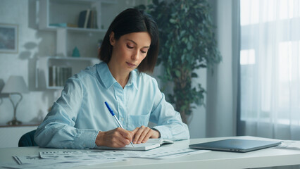 Business woman is writing on a notepad with a pen and using a laptop computer. Doing homework. Concept of lifestyle and work at home. Creative paper plan, idea or reminder for business goals