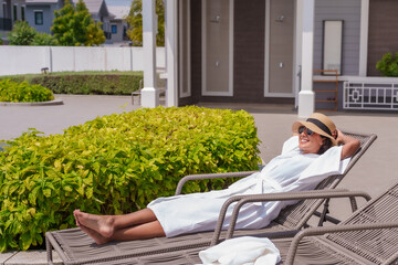 Beautiful Spanish woman wears a white robe after leaving the pool. Happily sunbathing on a chair by...