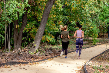 Fototapeta na wymiar Two female joggers pursuing their activity outdoors. Women running on the jogging track in the park. View from the back.